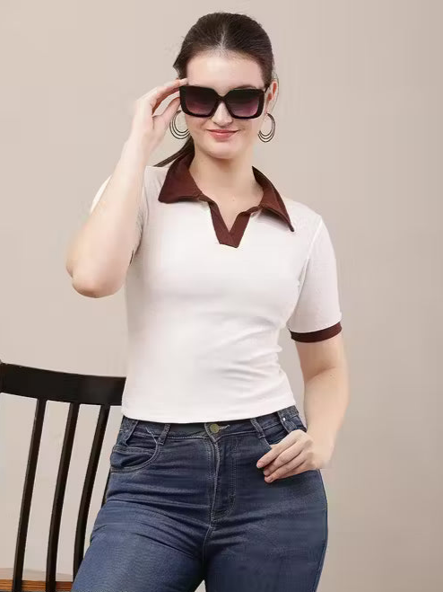 Woman wearing a white polo shirt with brown accents and blue jeans, holding sunglasses.